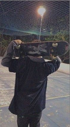 a man holding a skateboard over his head while standing on a tennis court at night