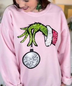 Get ready to make a bold and festive statement with our "Faux Sequin Grinch Hand Sweatshirt." This eye-catching sweatshirt features a playful graphic of the Grinch's hand dangling a disco ball, with faux sequins providing a dazzling and fun touch. Please note that the sequins are a graphic representation and are not real, ensuring comfort and ease of wear. Grinch Hand, Grinch Shirt, Grinch Hands, Sequin Design, Holiday Gathering, Disco Ball, Grinch, Festival Season, Graphic Tee