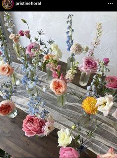 several vases filled with different colored flowers on a wooden table next to a wall