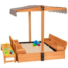 a wooden sandbox with an umbrella over it and two toys on the ground in front of it