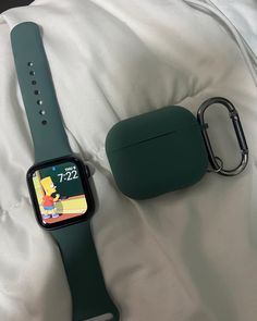 an apple watch sitting on top of a bed next to a green case and keychain