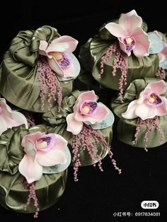 six pink and white flowers are in green satin bags on a black tablecloth background