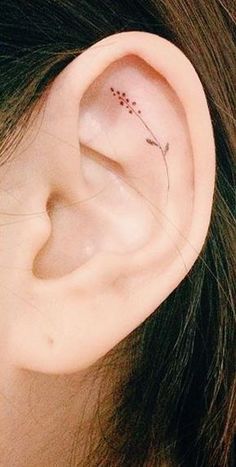 a woman's left ear has a tiny flower tattoo on it