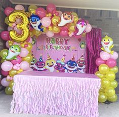 a birthday party with balloons and decorations on the front wall, along with a pink table cloth