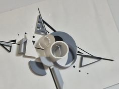 a clock that is on the side of a white wall with black and grey shapes