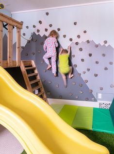 two children climbing up the side of a wall in a playroom with slides and climbing walls