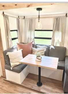 a couch and table in a small living room with wood flooring, windows, and curtains