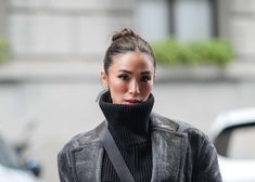 a woman wearing a black turtle neck sweater and grey coat is walking down the street