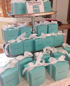 many blue boxes with white bows are stacked on a table in front of a cake