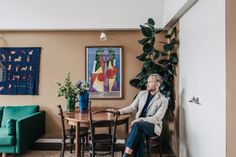 a man sitting at a table in front of a green couch next to a potted plant