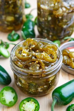 pickled jalapenos in jars on a wooden table with green peppers around them