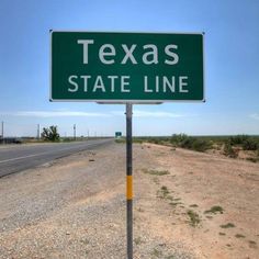 a green texas state line sign sitting on the side of a road next to a desert