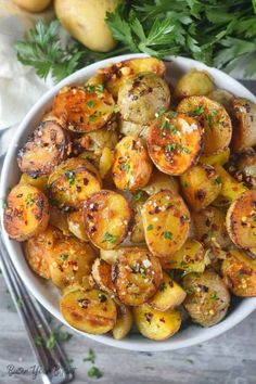 a white bowl filled with cooked potatoes and parsley on top of a wooden table