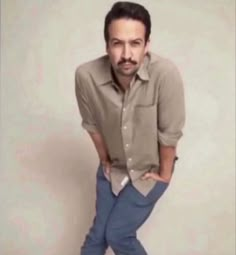 a man with his hands on his hips posing for the camera while wearing blue pants and a button up shirt