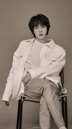 a young man sitting on top of a chair wearing a coat and pants with his hands in his pockets