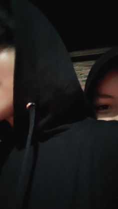 two people in black hoodies are looking at their cell phones and one person is wearing a hooded jacket