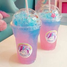 two pink and blue drinks with straws in them sitting on a table next to a teddy bear