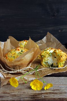 two muffins sitting on top of brown paper next to yellow flowers and wooden table