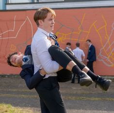 a man carrying another man on his back in front of a wall with graffiti behind him