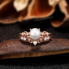 a white pearl and diamond ring sitting on top of a piece of wood next to flowers