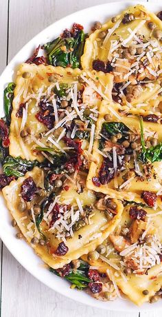 a white bowl filled with pasta and spinach covered in cheese on top of a wooden table