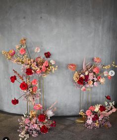 three tall vases with flowers on them against a gray wall in front of a concrete wall