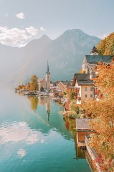 a lake with houses and mountains in the background, surrounded by trees that are changing colors