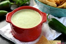 a red pot filled with white sauce next to tortilla chips and jalapenos