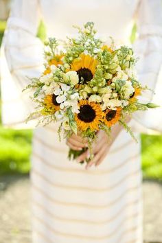 a bride holding a bouquet of sunflowers and greenery