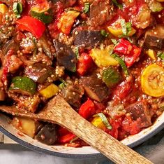 a pan filled with meat and vegetables on top of a table next to a wooden spoon