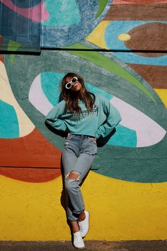 a woman standing in front of a colorful wall with her hands on her hips wearing sunglasses