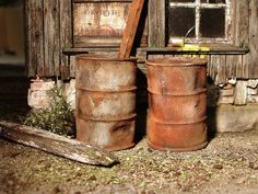 two rusty barrels sitting next to each other in front of a wooden building with an old window