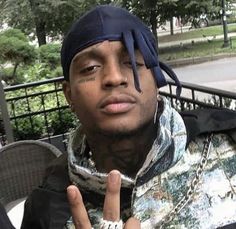 a young man with tattoos on his face sitting in a chair and making the peace sign