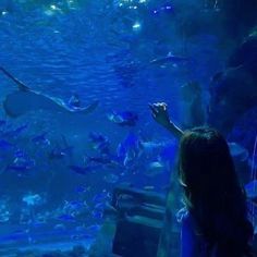 a woman standing in front of a large aquarium filled with fish