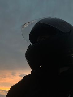 a person wearing a motorcycle helmet with the sun setting in the back ground behind them