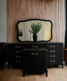 a black dresser with a mirror and vase on it