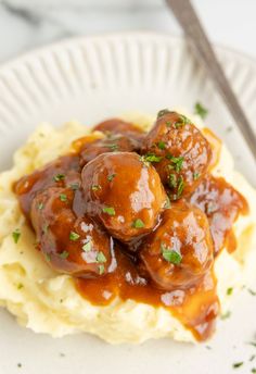 mashed potatoes topped with meatballs and gravy on a white plate next to a fork