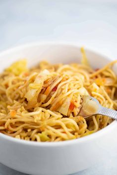 a white bowl filled with noodles and meat on top of a table next to a fork