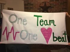 two people holding up a sign that says team one, one beat and one heart