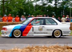 a white car with multicolored stripes driving down a road in front of a crowd