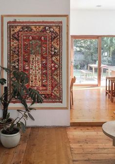 a living room filled with furniture and a rug hanging on the wall next to a potted plant