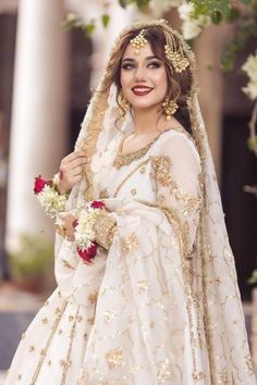 a woman wearing a white and gold bridal gown with flowers in her hair is posing for the camera