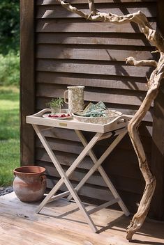 a small table with a cup on it next to a potted plant and tree branch