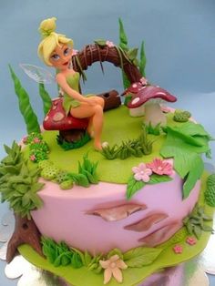 there is a cake with a fairy sitting on it's top and flowers around the base