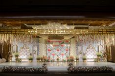 a stage set up for a wedding ceremony with flowers and chandeliers on it