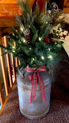 a christmas tree in a galvanine bucket with lights on the top and red ribbon