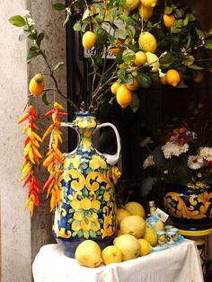 a table topped with yellow and blue vases filled with lemons next to potted plants