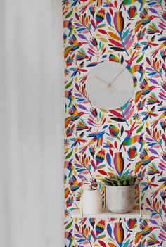 a colorful wall with a clock and plant on the shelf next to it, in front of a patterned wallpaper