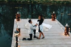 a man and woman standing on a dock next to each other with candles around them