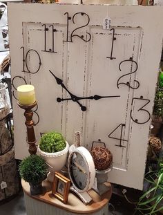 a white clock sitting on top of a table next to potted plants and candles